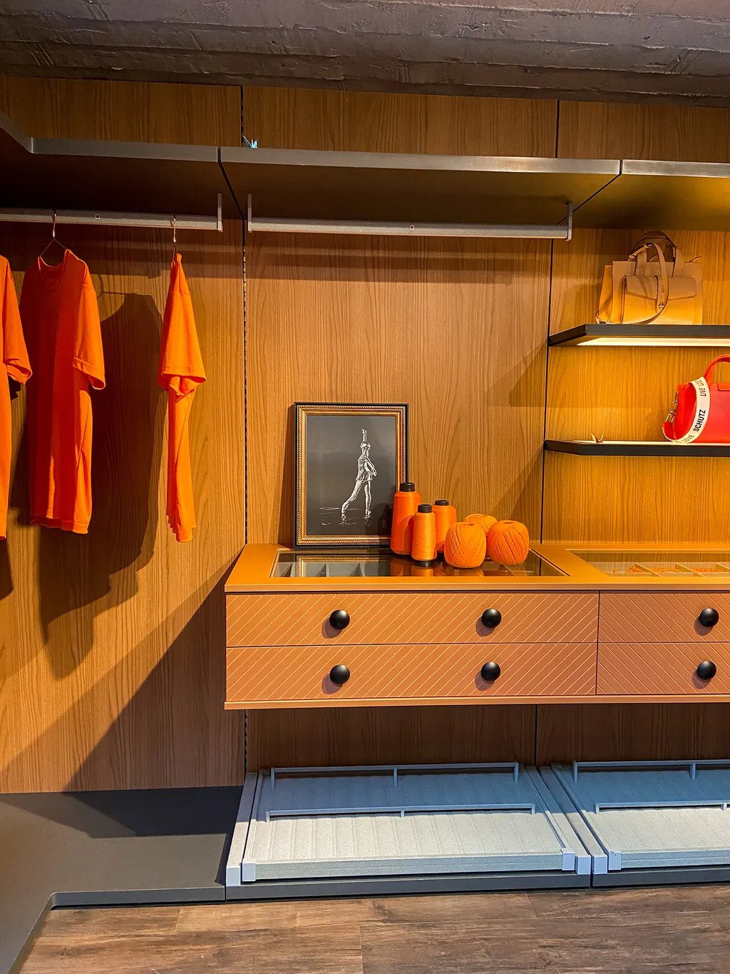Closet aberto com gavetões em terracota, prateleiras iluminadas e araras em lâmina de madeira.