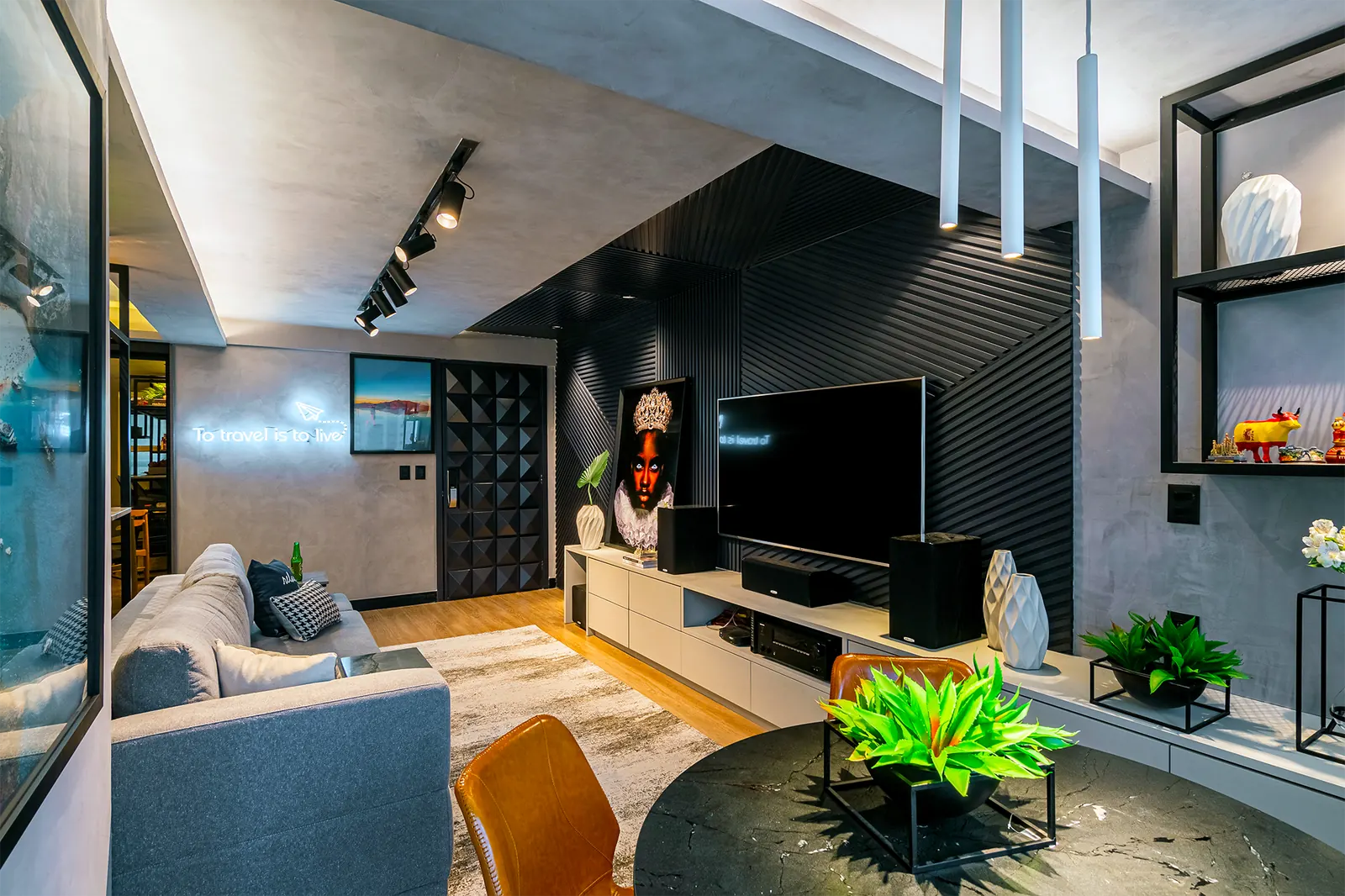 Vista ampla do living com painel ripado preto, trilho de spots e rack suspenso.